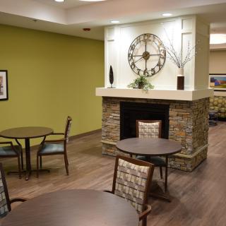 A cozy lobby featuring a stone fireplace with a large decorative clock above, surrounded by small tables and chairs.