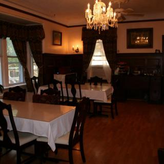 A cozy dining room with traditional decor, featuring a chandelier, wood furniture, and elegant curtains.