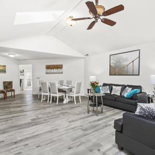 A modern and spacious living room with a dining area, featuring hardwood floors and a ceiling fan.
