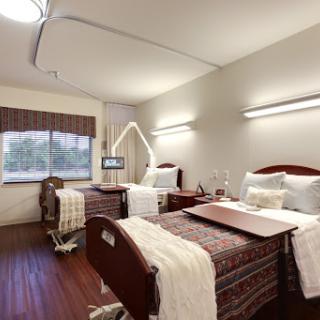 A spacious and well-lit hospital patient room equipped with two beds and modern amenities.