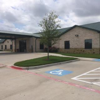 A brick building with a covered entrance and handicap parking spaces in the foreground, set under a cloudy sky.
