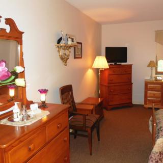 A cozy bedroom with wooden furniture, including a dresser with a mirror, a chair, and a television.