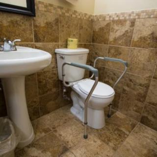 A bathroom with a toilet equipped with handrails for accessibility and a sink, featuring tiled walls and floors.