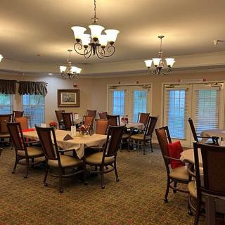 A cozy dining room with multiple tables and chairs arranged under elegant chandeliers.