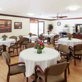 A community dining room with round tables and chairs, decorated with flowers.