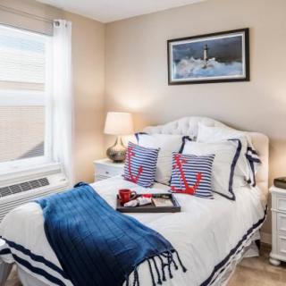 A cozy bedroom with a nautical theme, featuring a neatly made bed adorned with anchor-patterned pillows and a blue throw blanket.