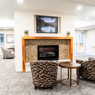 A cozy living room with a modern fireplace, flanked by two patterned armchairs and a small coffee table.