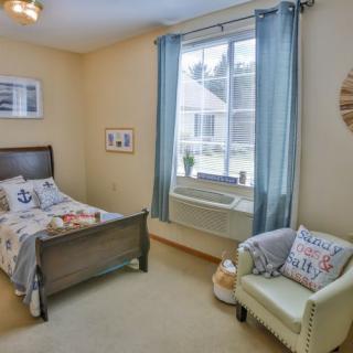 A cozy child's bedroom featuring a bed with nautical-themed bedding, a window with blue curtains, and a comfortable chair.