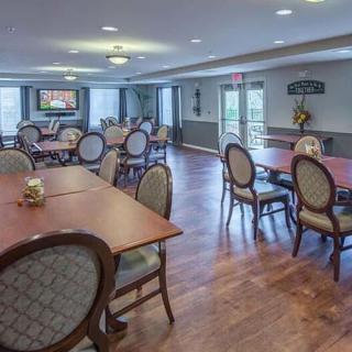 A spacious dining room with multiple tables and chairs, featuring a wooden floor and a chandelier.