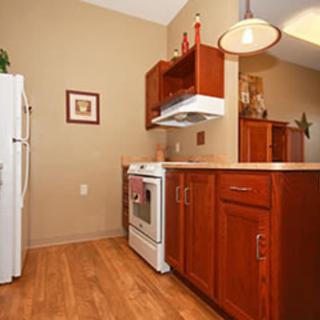 A cozy kitchen with wood cabinetry, featuring an oven and refrigerator, accented by a pendant light.