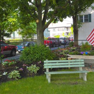A peaceful garden scene with a bench, flowers, and an American flag.