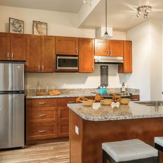 A modern kitchen with wooden cabinets, stainless steel appliances, and a central island with stools.