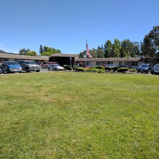 A wide view of a grassy area in front of a building with several parked cars under a clear blue sky.