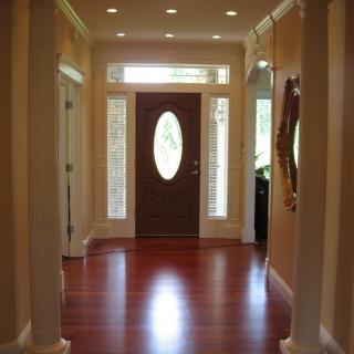 A well-lit hallway with a wooden floor and an oval glass front door.