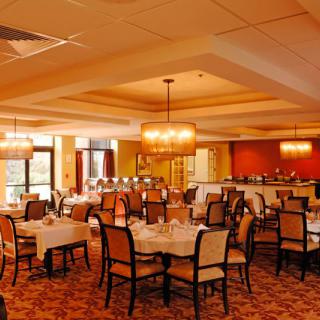 A spacious and elegant restaurant dining room with neatly arranged tables and chairs, illuminated by warm chandeliers.