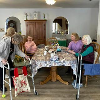 A group of elderly women gathered around a table, engaging in conversation at a nursing home.