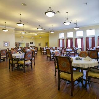 A spacious dining area with neatly arranged tables and chairs, featuring elegant lighting and wooden floors.