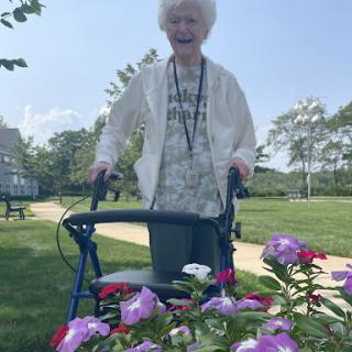 An elderly woman enjoying a sunny day in the park, surrounded by colorful flowers.