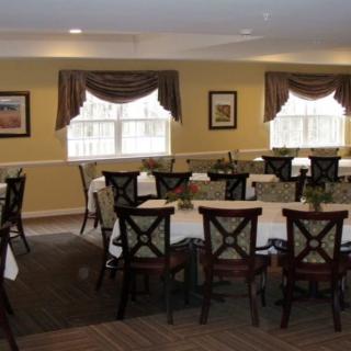 A neatly arranged dining room with multiple tables and chairs, featuring large windows with curtains.