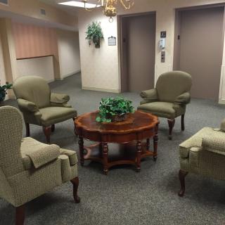 A cozy waiting area with green upholstered chairs and a wooden coffee table.