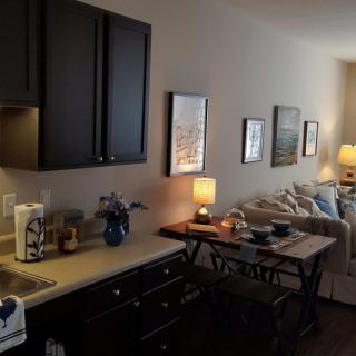 A cozy living space featuring a small dining area and kitchenette, adorned with artwork and soft lighting.