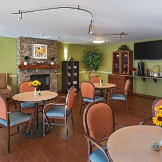 A cozy dining area with neatly arranged tables and chairs, featuring a fireplace and warm decor.