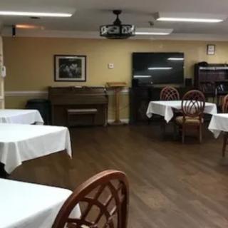 An indoor dining area with tables covered in white tablecloths, a piano, and a television.