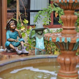 Garden scene with decorative statues of children near a fountain.