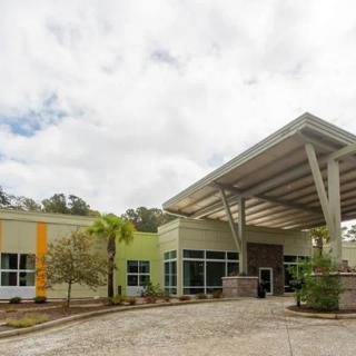 A modern building with a prominent entrance and covered walkway under a cloudy sky.