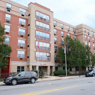 Street view of a multi-story apartment building with cars parked in front.