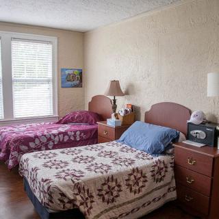 A cozy bedroom featuring two twin beds with patterned bedspreads, complemented by bedside tables and lamps, illuminated by natural light from a nearby window.