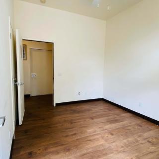 An empty room with wooden flooring and white walls, featuring an open door leading to another space.