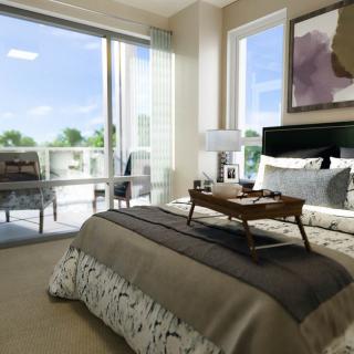 A modern bedroom featuring a neatly arranged bed with a breakfast tray, large windows allowing natural light, and access to a balcony.