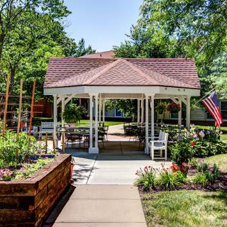 A charming gazebo surrounded by a well-maintained garden, featuring a paved walkway and seating area.