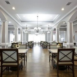 A spacious and elegantly designed dining room with chandeliers, columns, and neatly arranged tables and chairs.