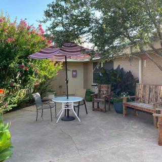 A cozy patio with a table and chairs under an umbrella, surrounded by lush greenery.