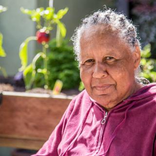 An elderly woman sitting outside in a garden on a sunny day.