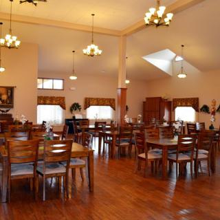 An empty dining hall with wooden tables and chairs, well-lit by chandeliers.