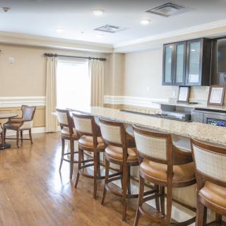 A spacious kitchen area featuring a long countertop with bar stools and wooden flooring, complemented by cabinetry and natural lighting.