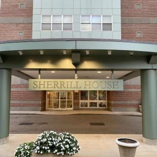 The entrance to a building with the sign 'Sherrill House' displayed above, featuring architectural details and potted flowers.