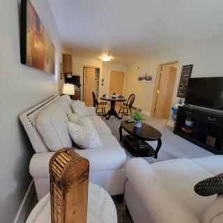 A cozy living room featuring a white sofa, coffee table, and television, with a dining area in the background.