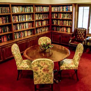 A cozy library room with wooden bookshelves, a round table, and upholstered chairs.