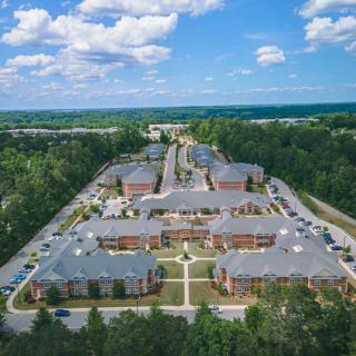 Aerial view of a large apartment complex surrounded by trees under a partly cloudy sky.
