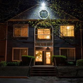 A house at night with illuminated windows and entrance, surrounded by trees.