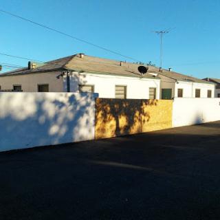 A residential building surrounded by a white fence, illuminated by sunlight in an urban setting.