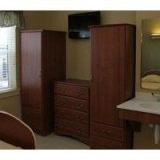 A room featuring wooden wardrobes, a dresser, a wall-mounted television, and a mirror.