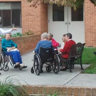 A group of elderly individuals socializing in wheelchairs outside a building.