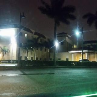 A nighttime view of a well-lit building surrounded by palm trees.