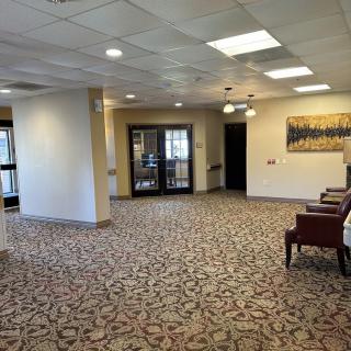 A neatly arranged lobby area featuring chairs, patterned carpet, artwork on the wall, and ceiling lights.