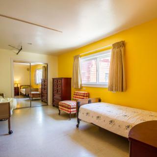 A cozy bedroom with bright yellow walls, featuring a single bed and simple furnishings.